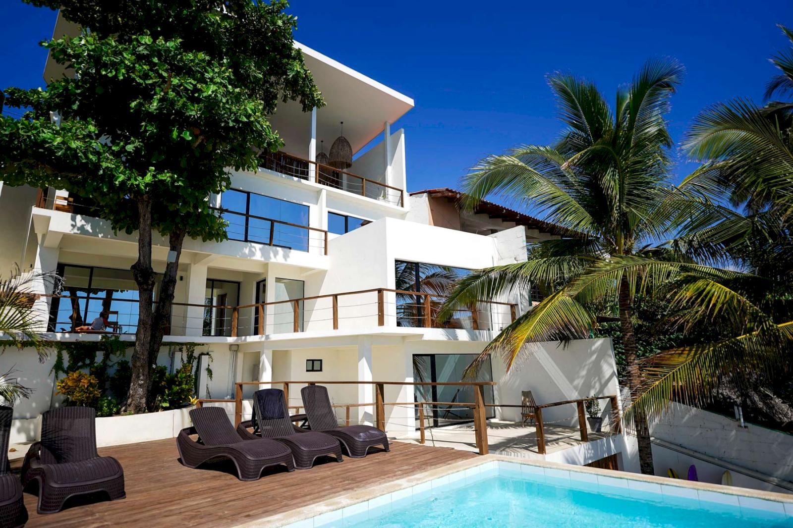 Vitt hotell med palmer och pool.