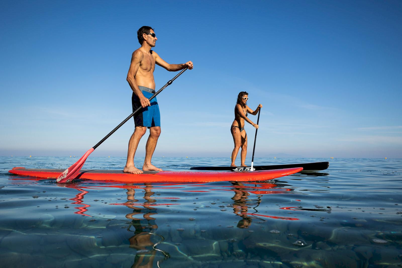 kvinna och man står på varsin stand up paddle board på vattnet 